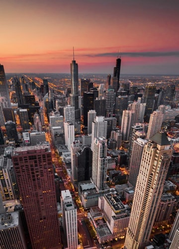 A wide angle arial shot of a city during sunset, looking down
                     upon the tall buildings and busy life below