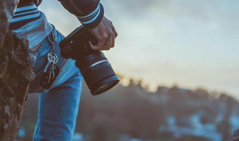 A young male photographer standing on top of a hill, looking out onto a snowy mountain range blurred out in the background