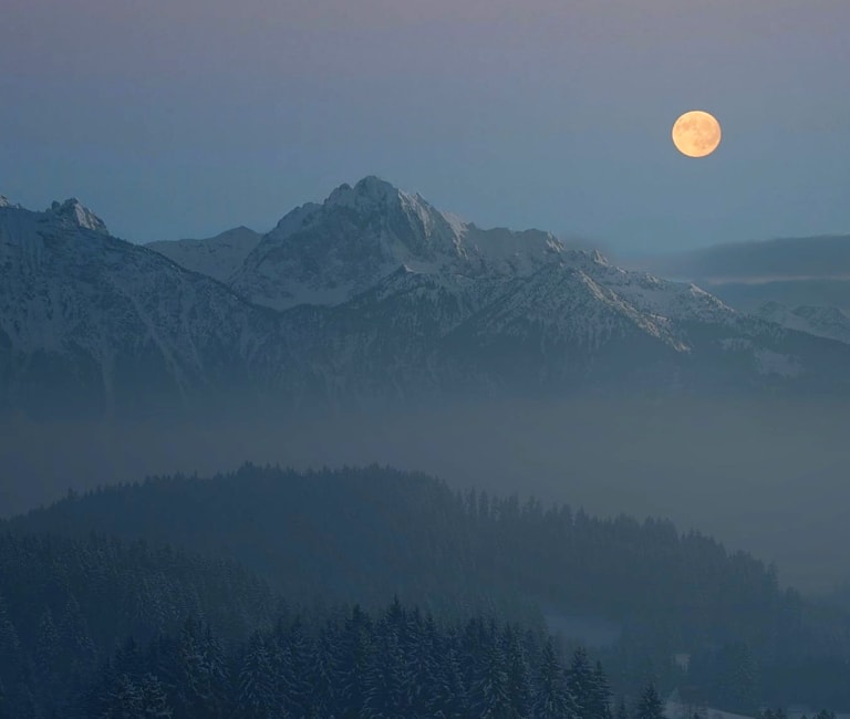 Ultra wide shot of a snowy mountain range with the sun setting in the background