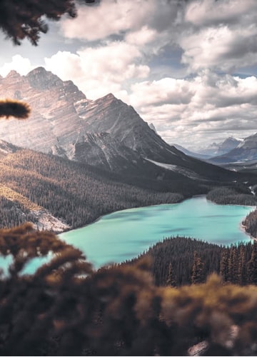 Wide shot of a clear green lake, centrally positioned between some mountains and hilly forests